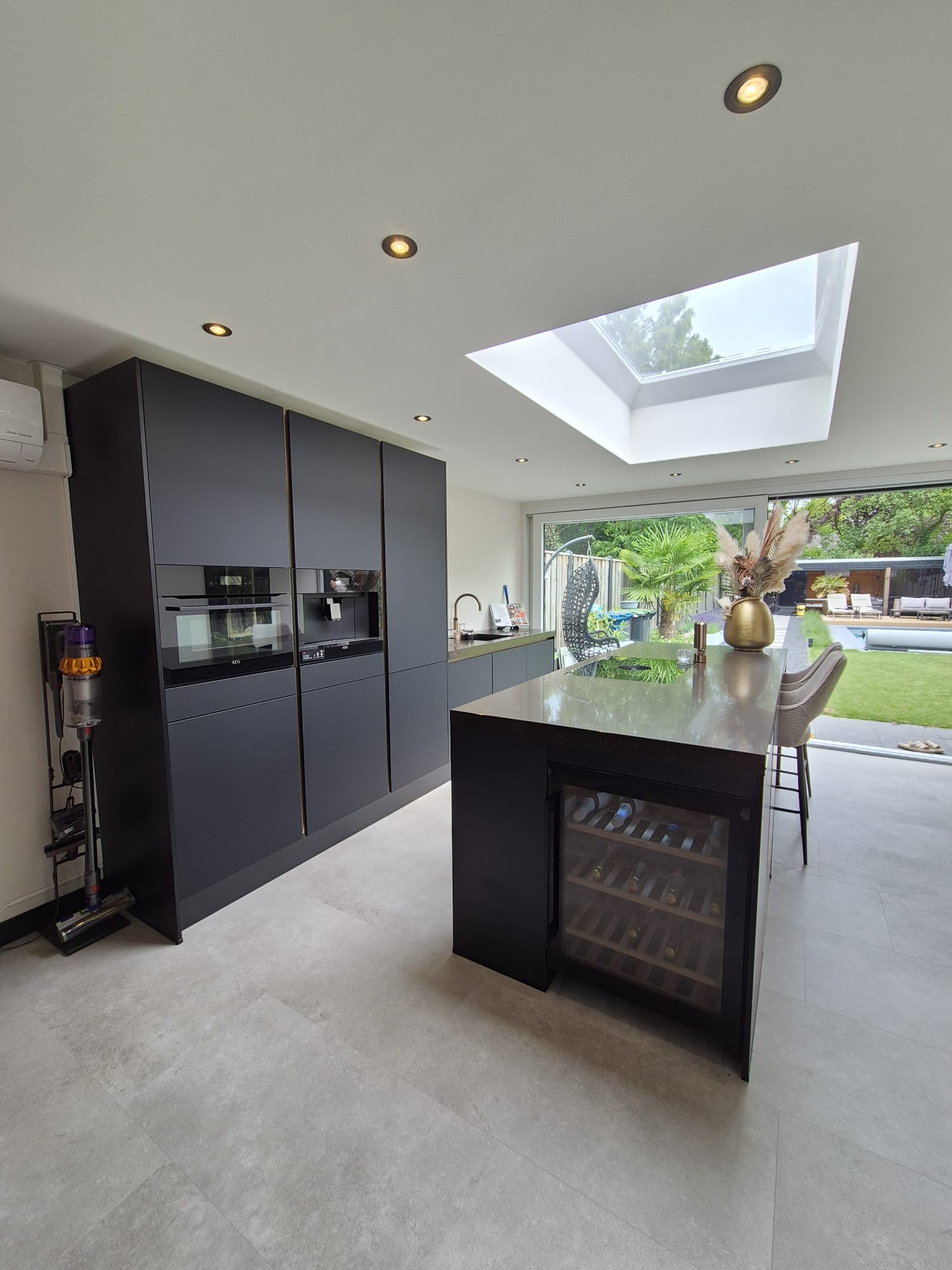 Modern kitchen renovation by Construxx in Eindhoven featuring a luxury dark kitchen with island, skylight, and wine cooler